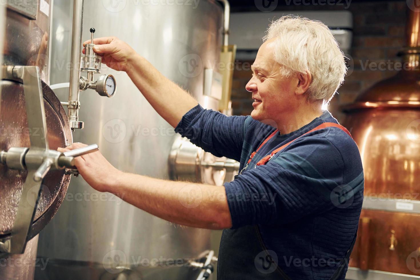 estilo retro. el anciano está parado en el almacenamiento con equipo para cerveza foto