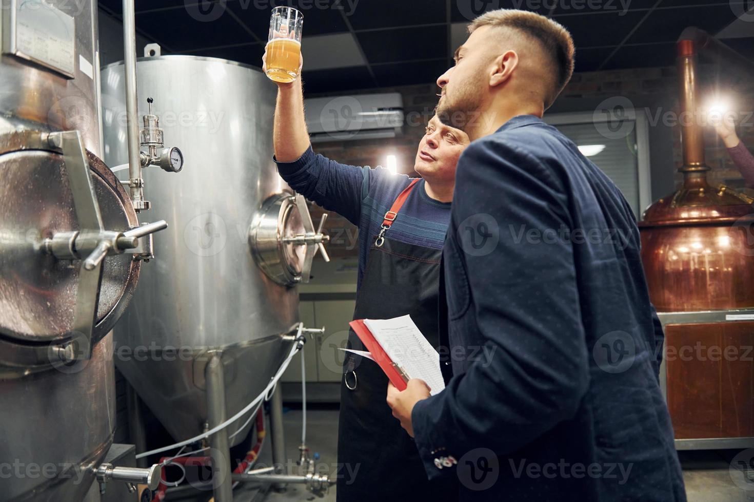 Senior man and young worker with document is standing in the storage beer room photo
