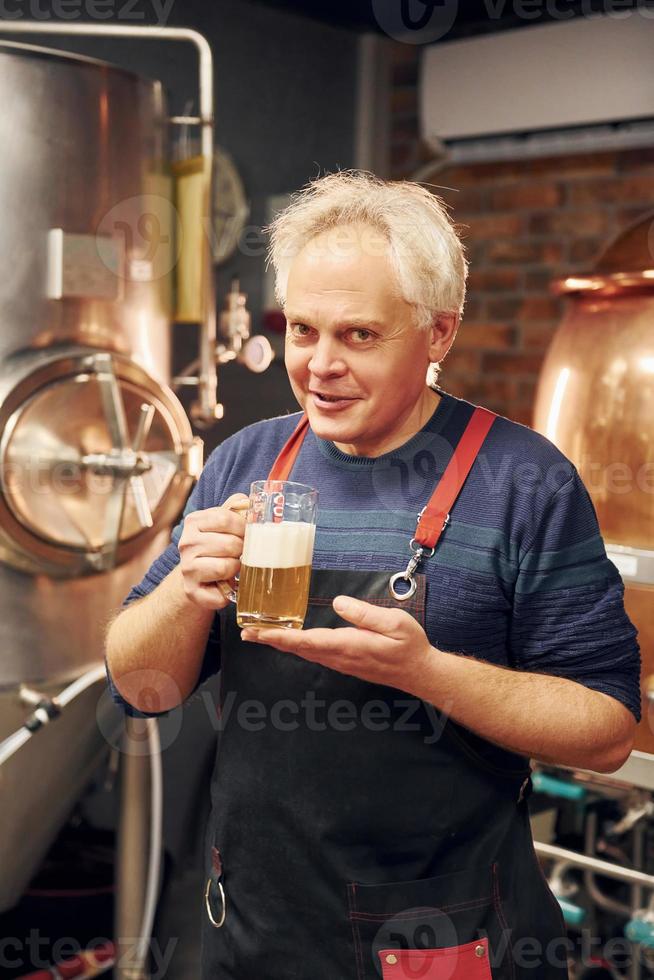 el anciano está parado en el almacenamiento con equipo para cerveza foto