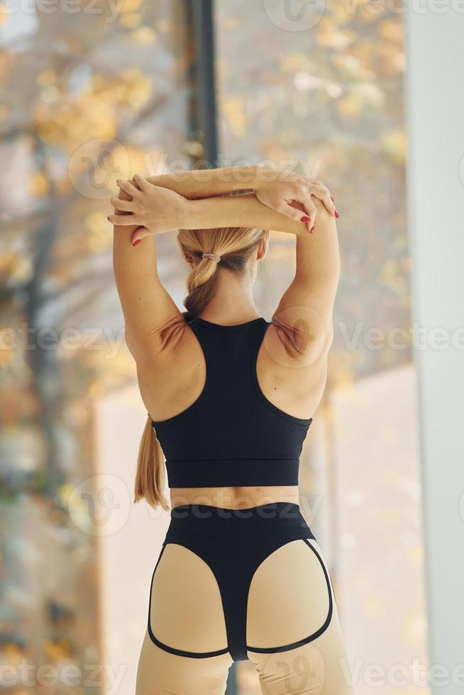 Standing against window. Woman in sportive clothes doing yoga indoors photo