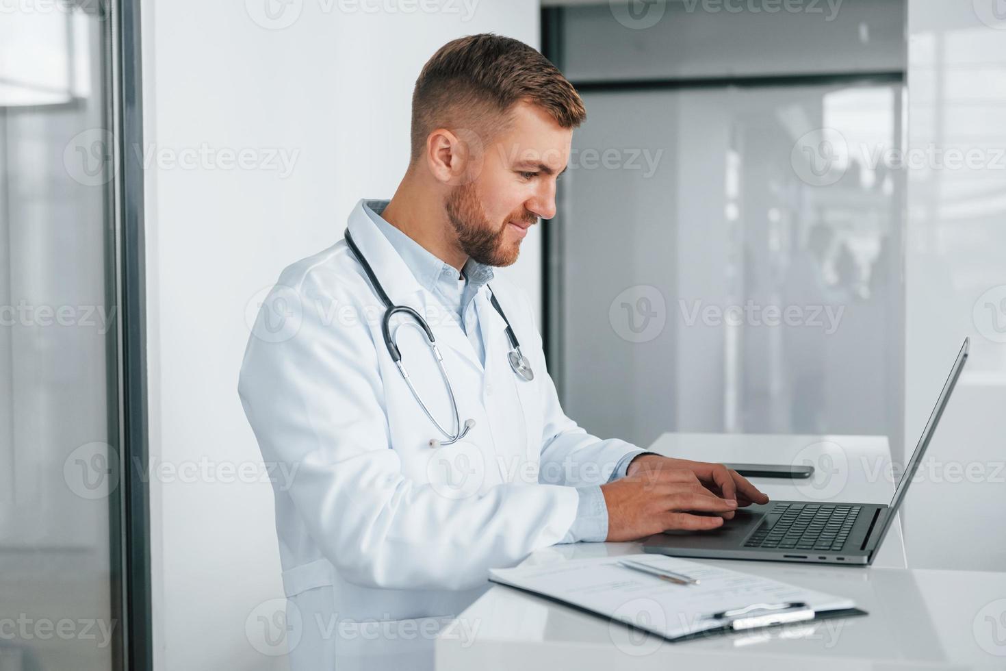 Using laptop. Professional medic in white coat is in the clinic photo