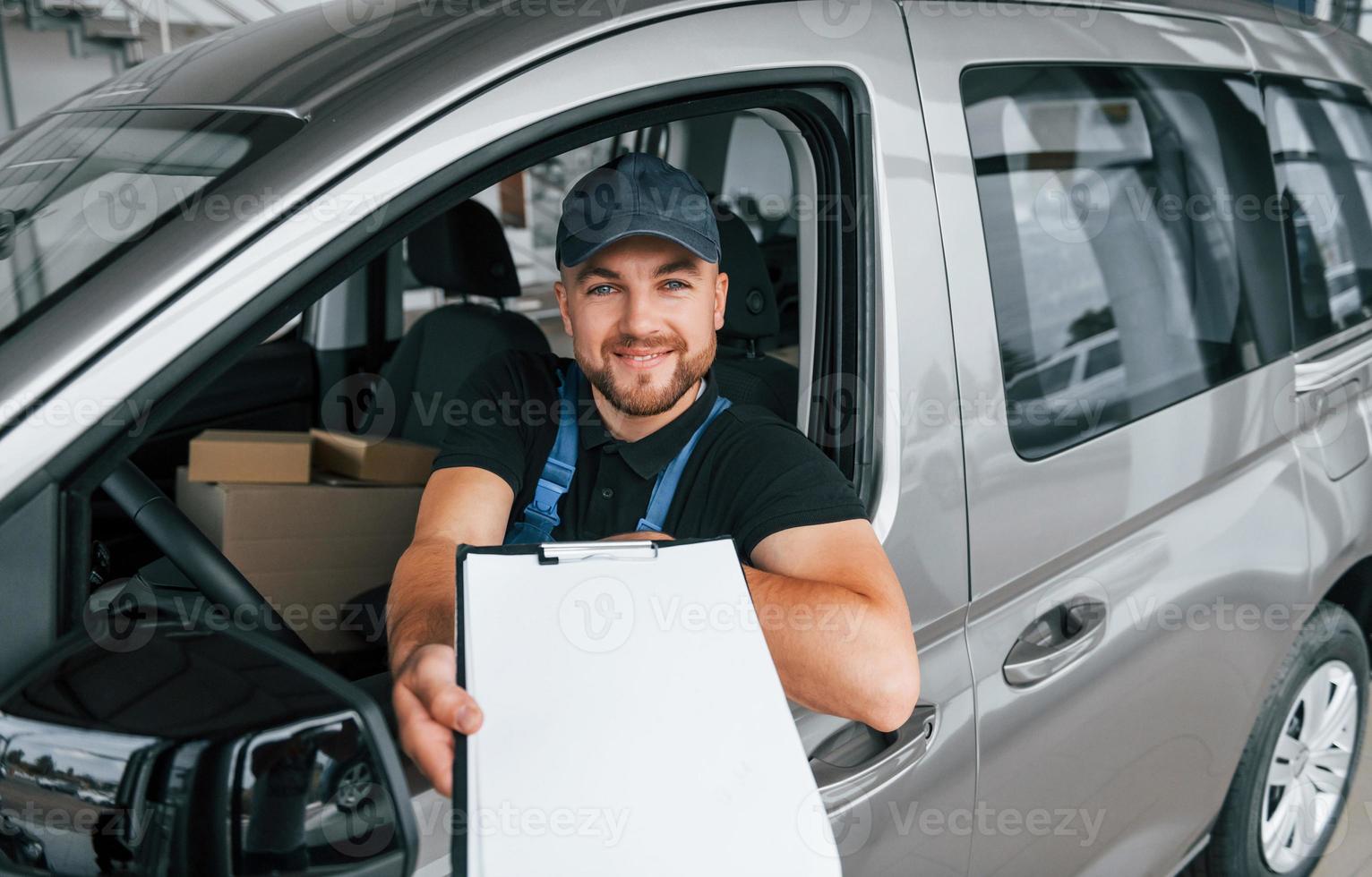 With vehicle. Delivery man in uniform is indoors with car and with order photo