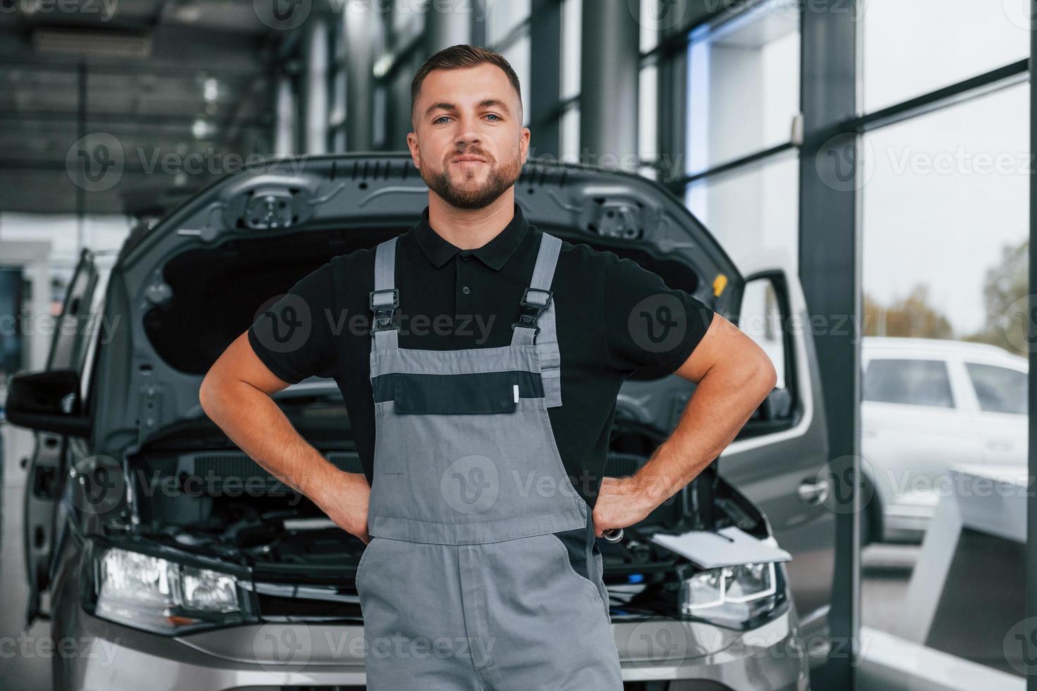 de pie contra el coche. el hombre de uniforme está trabajando en el autosalón durante el día foto