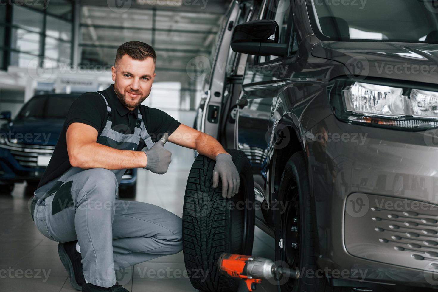 Changing of the tires. Man in uniform is working in the autosalon at daytime photo