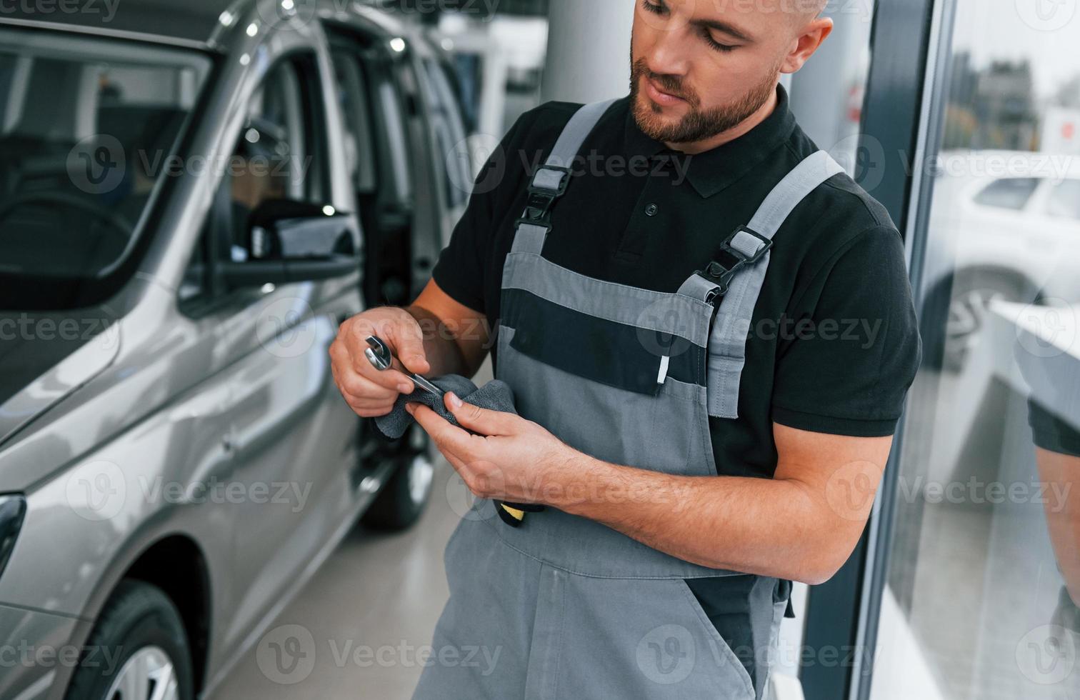 Tools in hands. Man in uniform is working in the autosalon at daytime photo