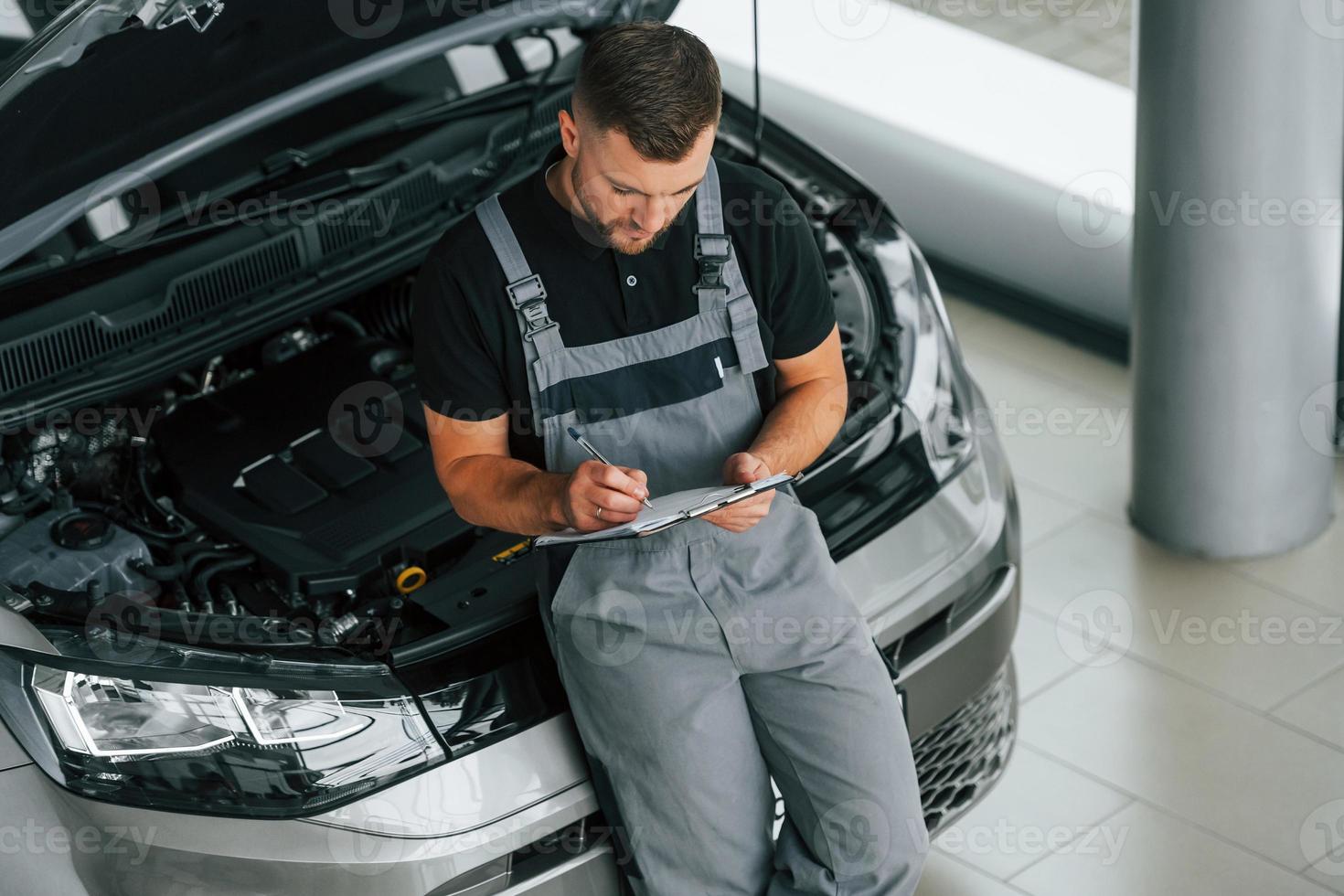 Near the car. Man in uniform is working in the autosalon at daytime photo