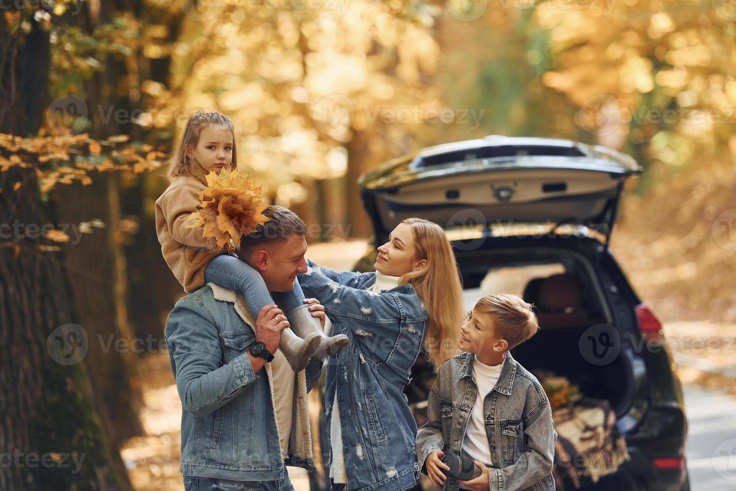 Near car with open trunk. Happy family is in the park at autumn time together photo