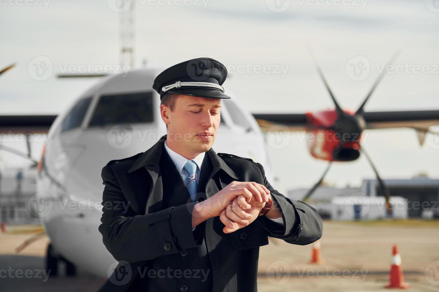 comprobando la hora. piloto con uniforme negro formal está parado al aire libre cerca del avión foto