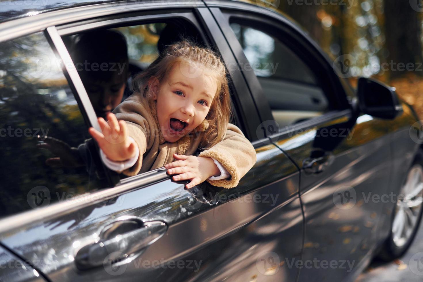 Little girl sitting in the black automobile and looking through the window photo