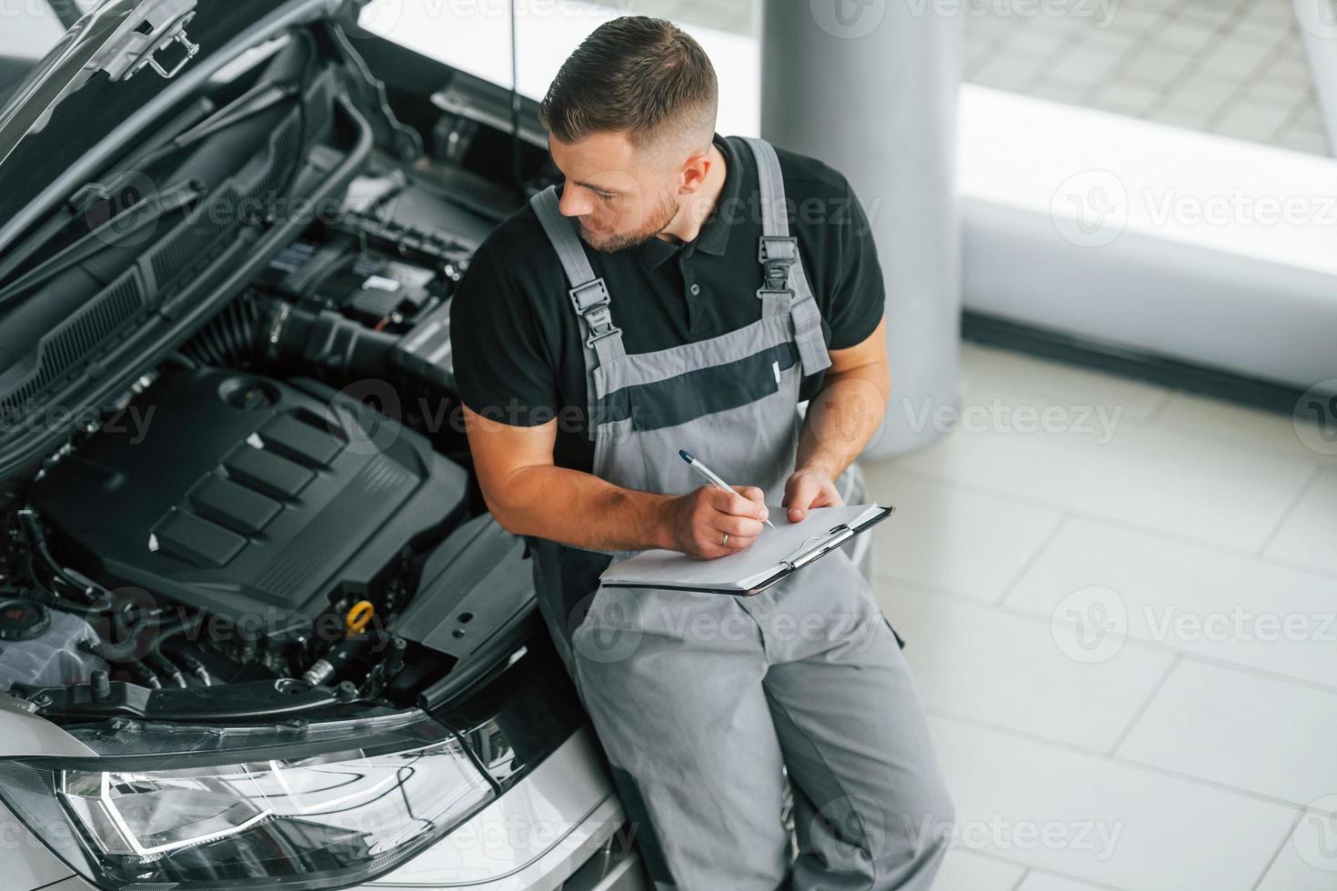 Engine repair. Man in uniform is working in the autosalon at daytime photo