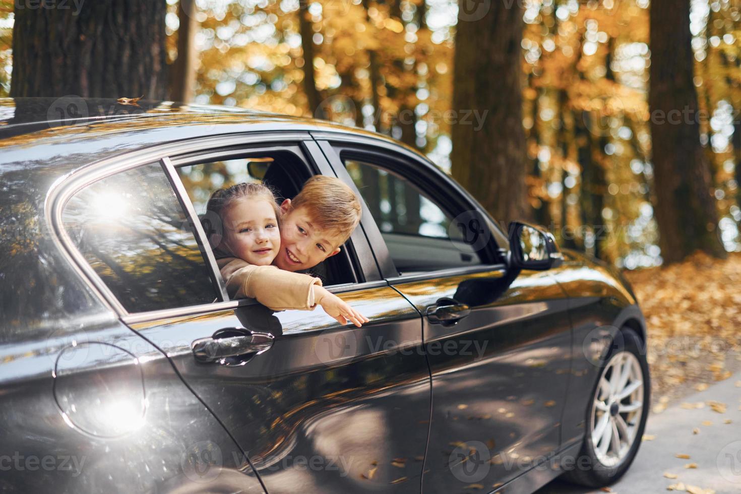 Little girl with her brother sitting in the car and looking through the opened window photo