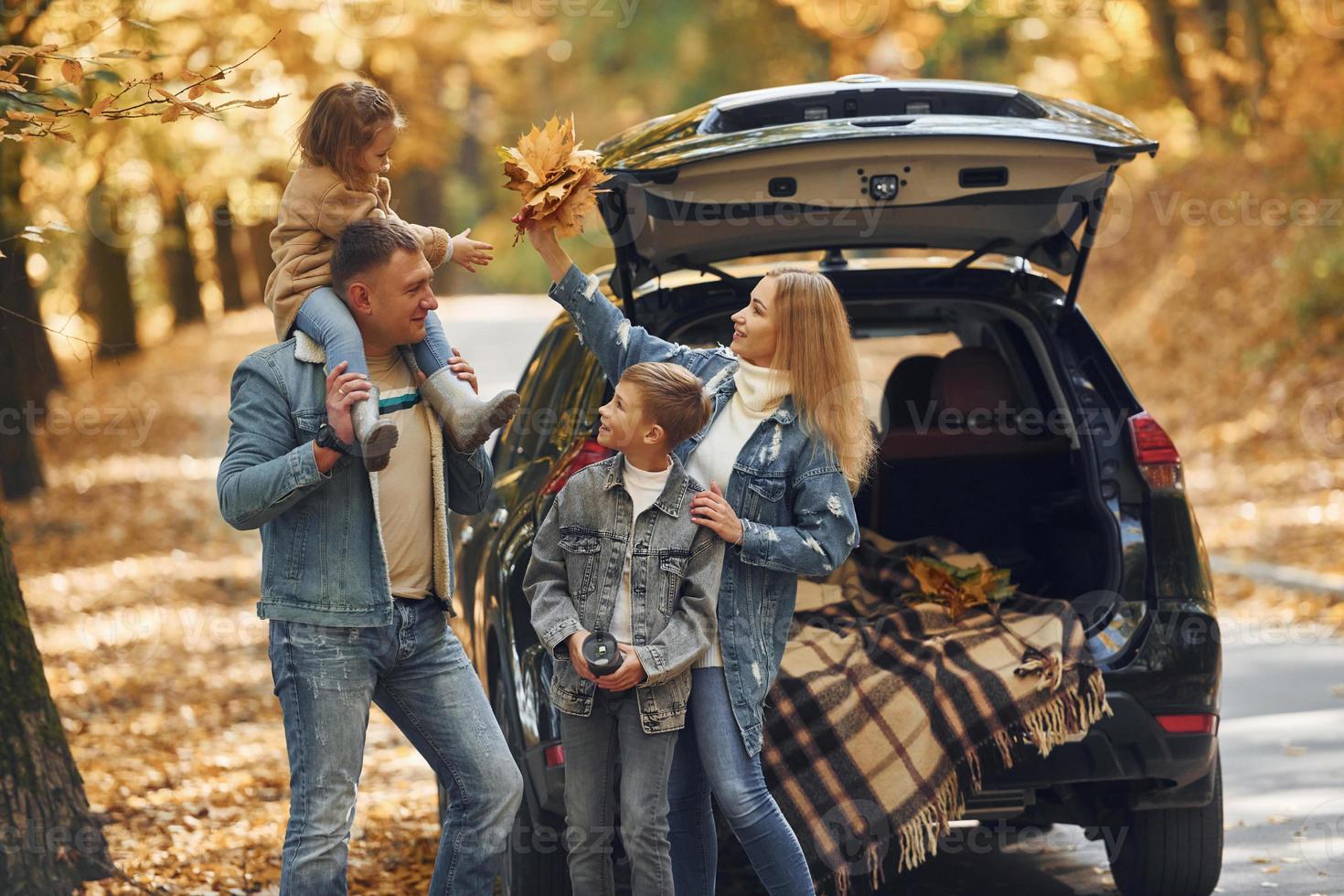 Near car with open trunk. Happy family is in the park at autumn time together photo