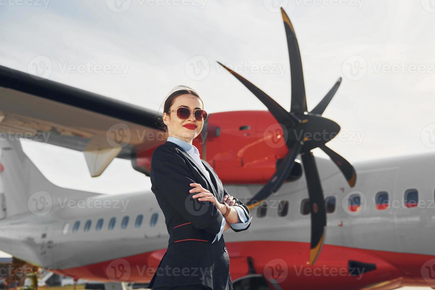 una joven azafata que está vestida de negro formal está parada al aire libre cerca del avión foto