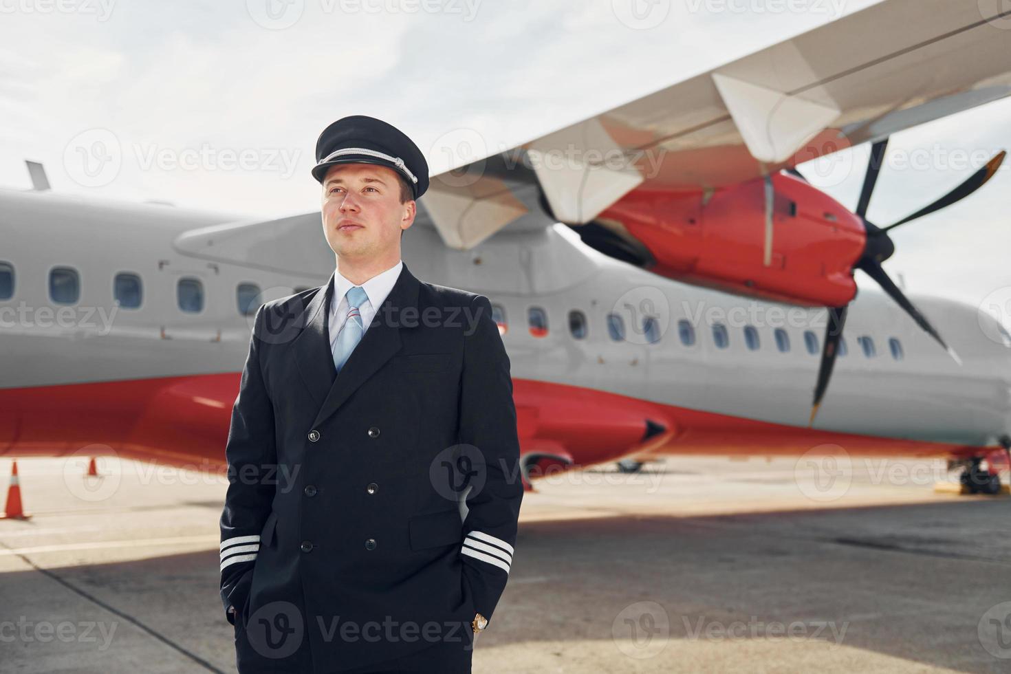 piloto con uniforme negro formal está parado al aire libre cerca del avión foto