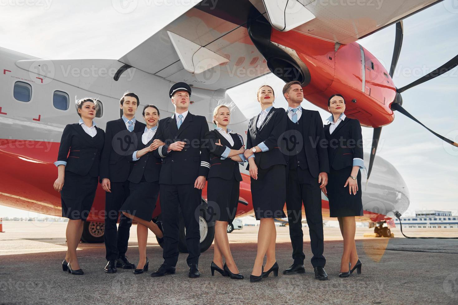 cerca del avión. tripulación de trabajadores del aeropuerto con ropa formal de pie juntos al aire libre foto