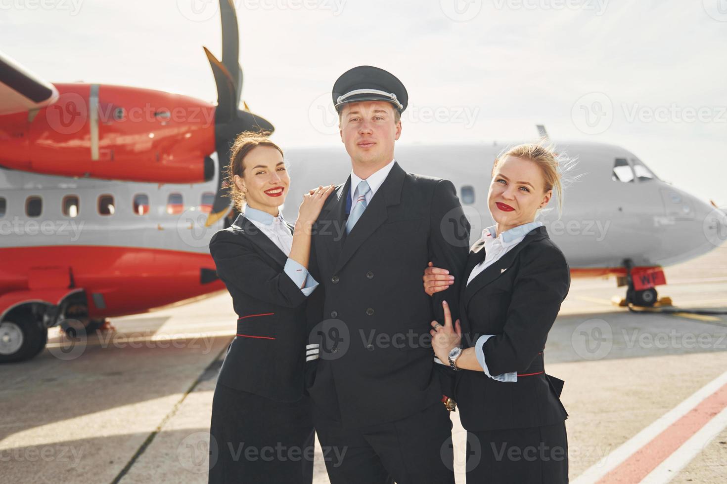 Pilot and two stewardesses. Crew of airport and plane workers in formal clothes standing outdoors together photo