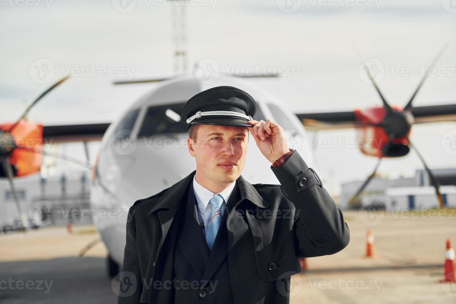 Pilot in formal black uniform is standing outdoors near plane photo