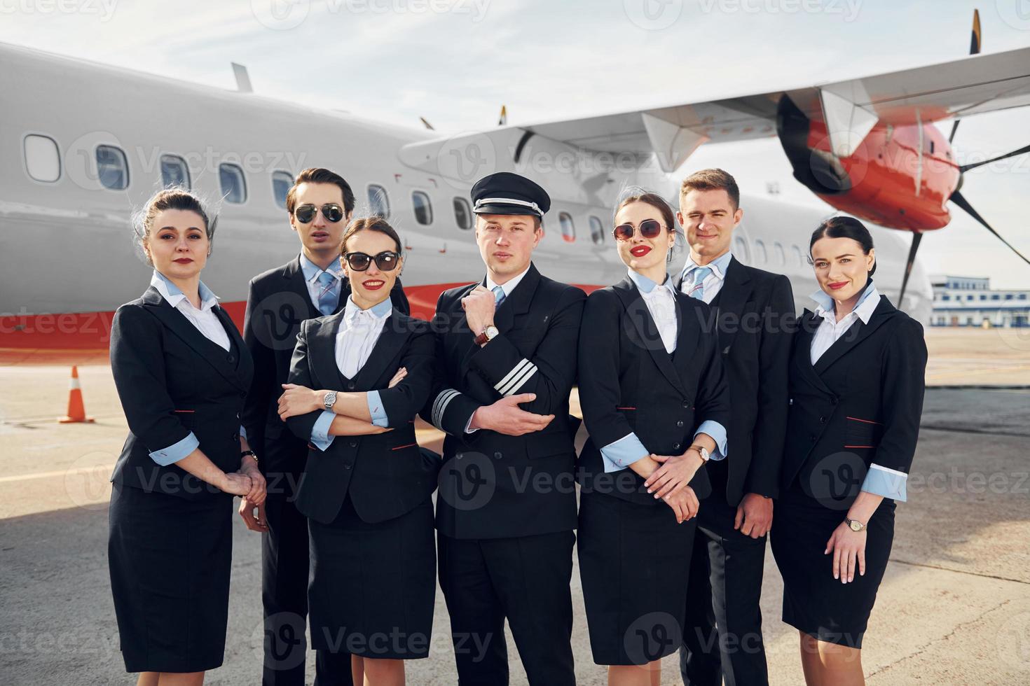 Posing for a camera. Crew of airport and plane workers in formal clothes standing outdoors together photo