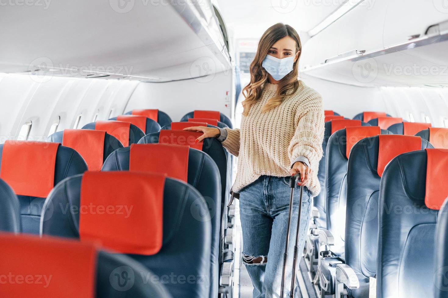 Holding lugagge. Young female passanger in casual clothes is in the plane photo