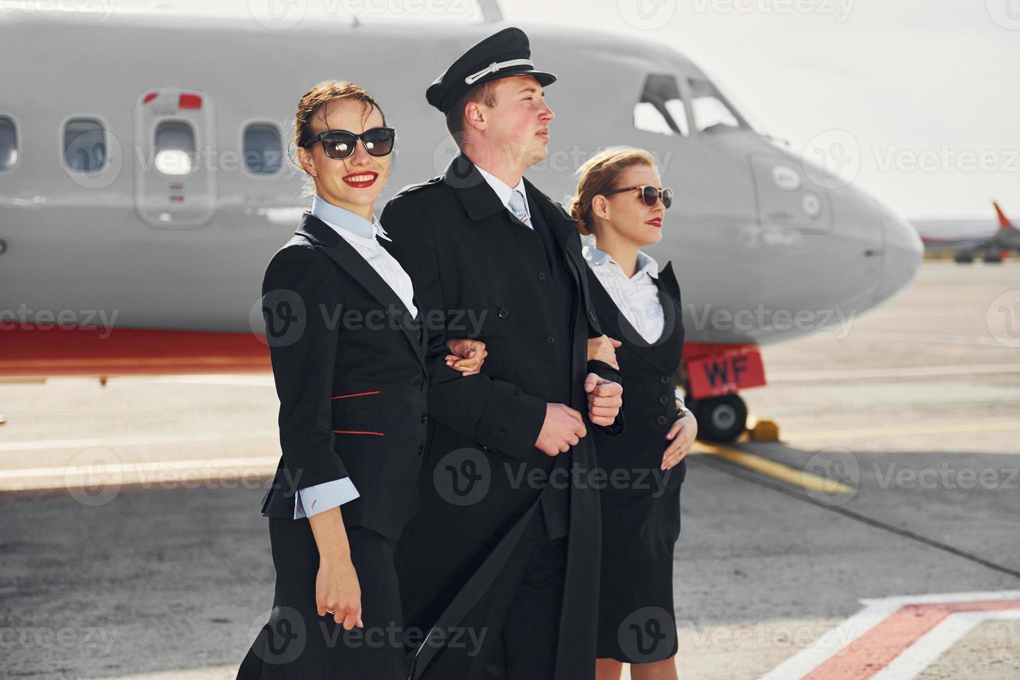 Three people. Crew of airport and plane workers in formal clothes standing outdoors together photo