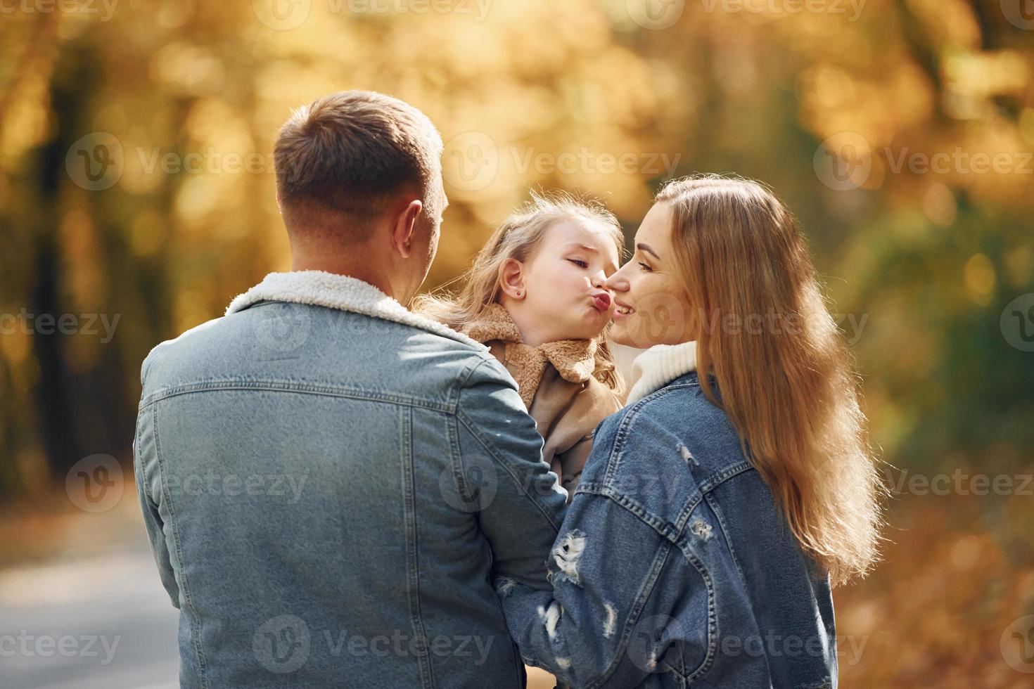 Little girl with her parents. Happy family is in the park at autumn time together photo