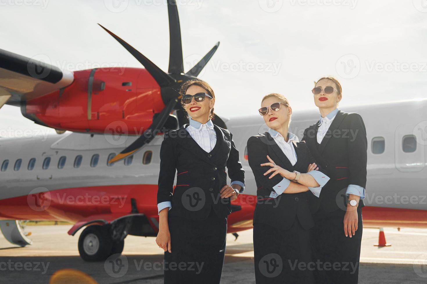 tres azafatas. tripulación de trabajadores del aeropuerto y del avión con ropa formal de pie juntos al aire libre foto