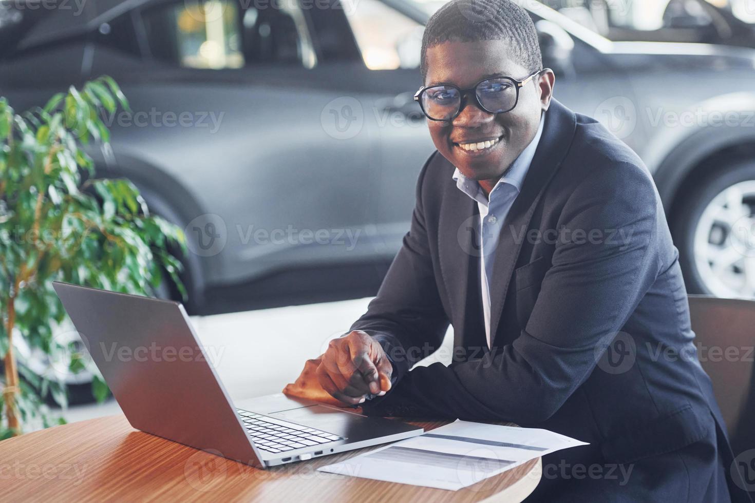 Office worker is sitting in autosalon by table with laptop photo