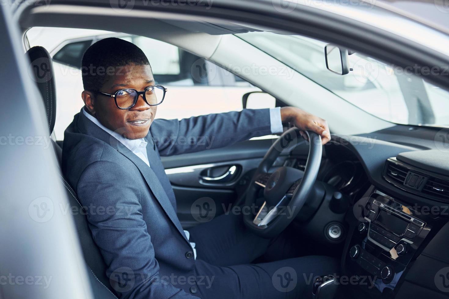 Side view. Young african american businessman in black suit is in the automobile photo