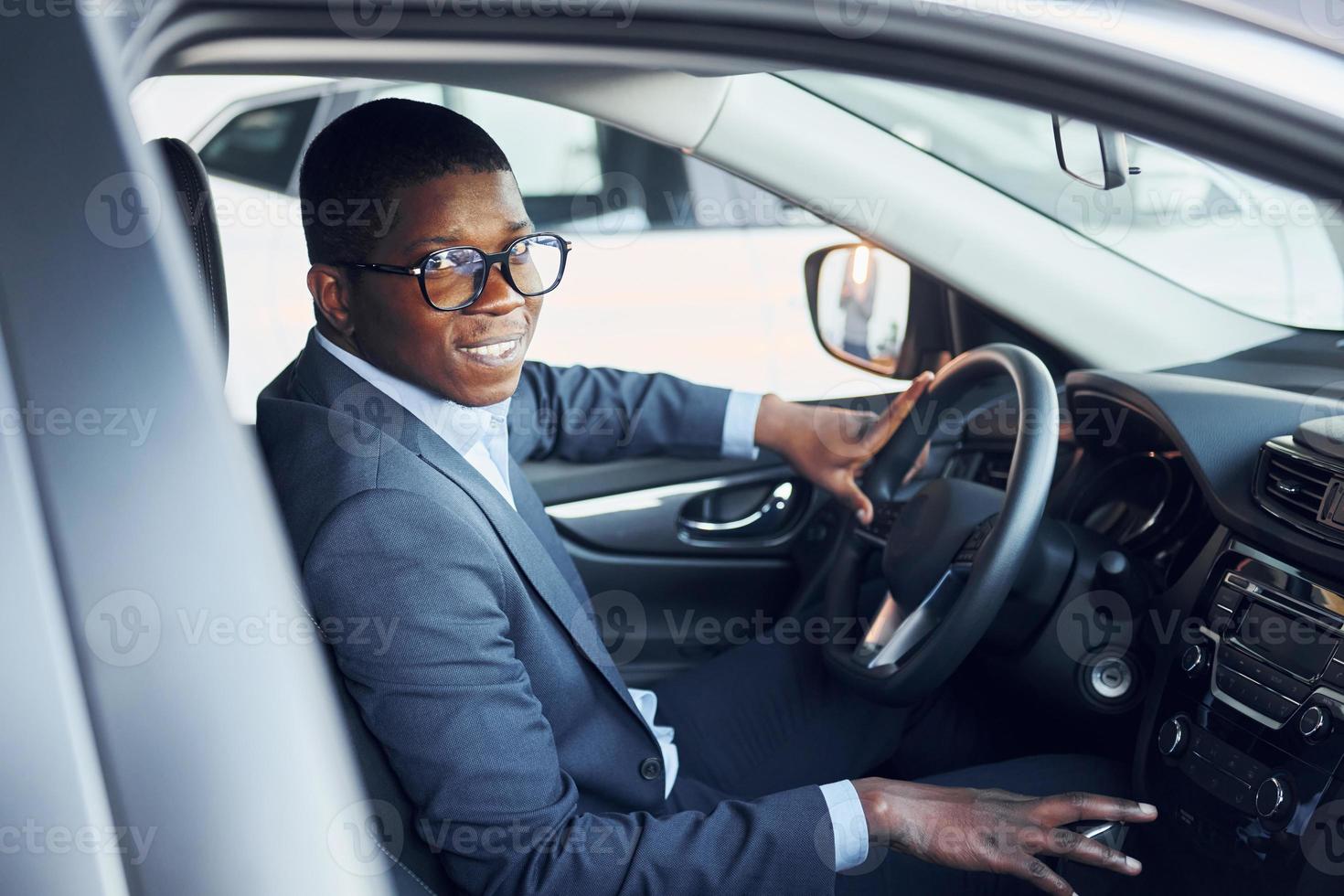 Side view. Young african american businessman in black suit is in the automobile photo