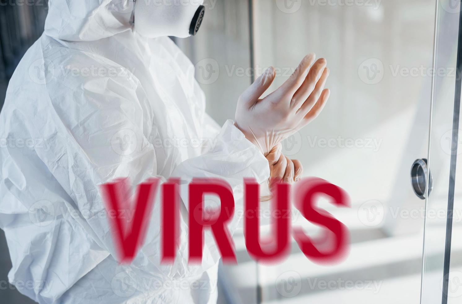 Red virus word. Nurse in protective uniform, mask and glasses standing indoors photo