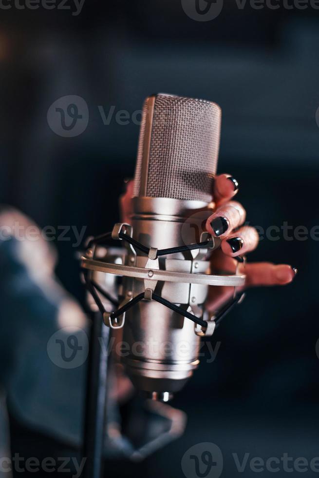 vista de cerca del micrófono. joven y bella intérprete femenina ensayando en un estudio de grabación foto