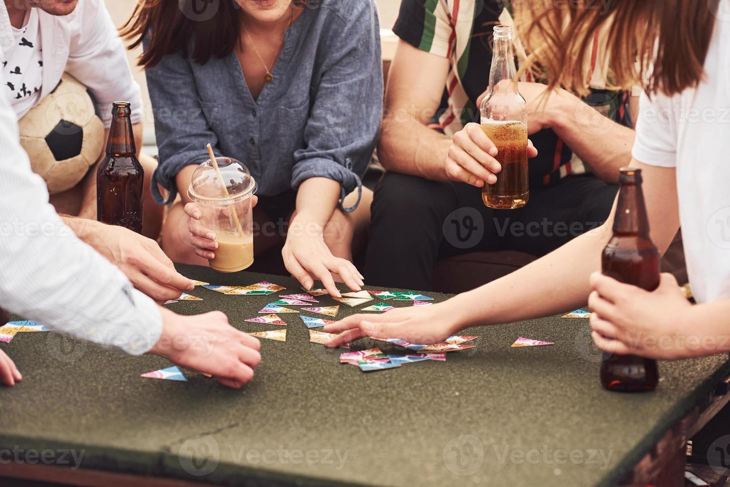 Playing game and sitting by the table. Group of young people in casual clothes have a party at rooftop together at daytime photo