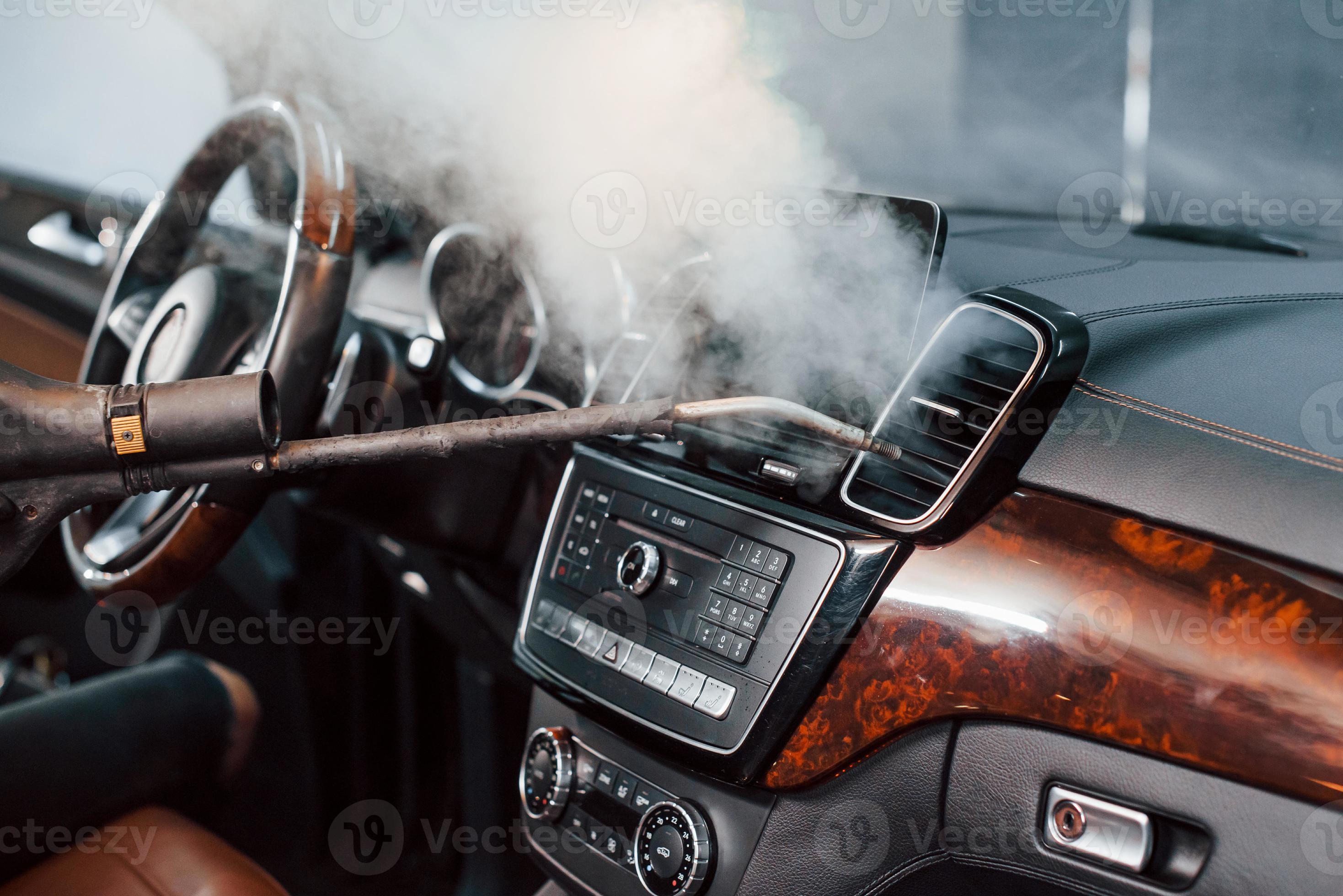 Modern black automobile get cleaned inside by steam equipment by worker