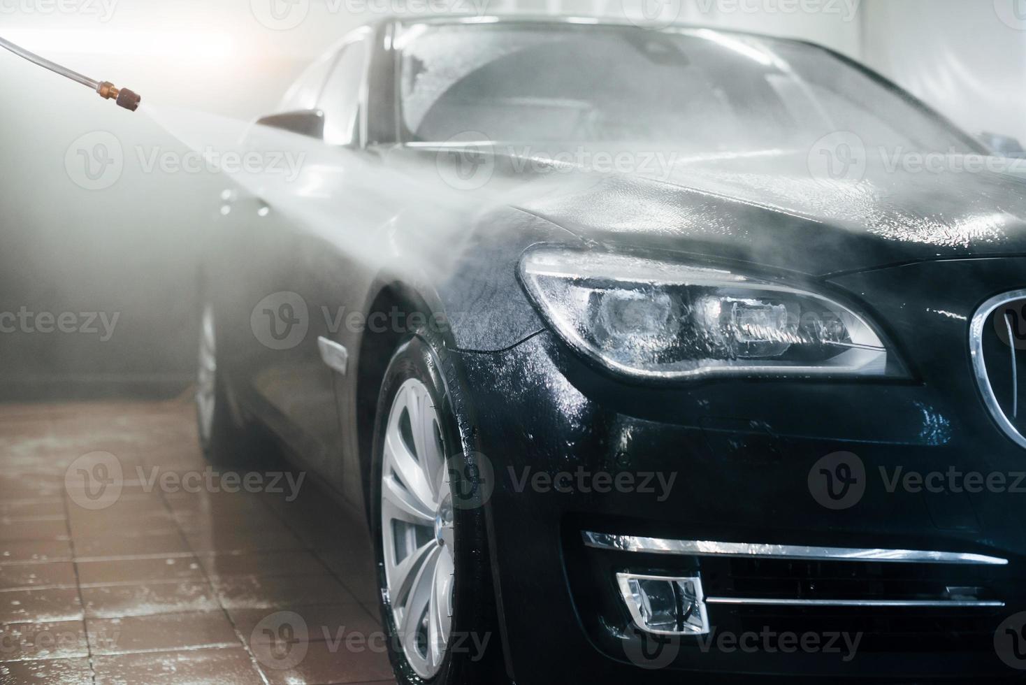 High pressured water. Modern black automobile get cleaned inside of car wash station photo