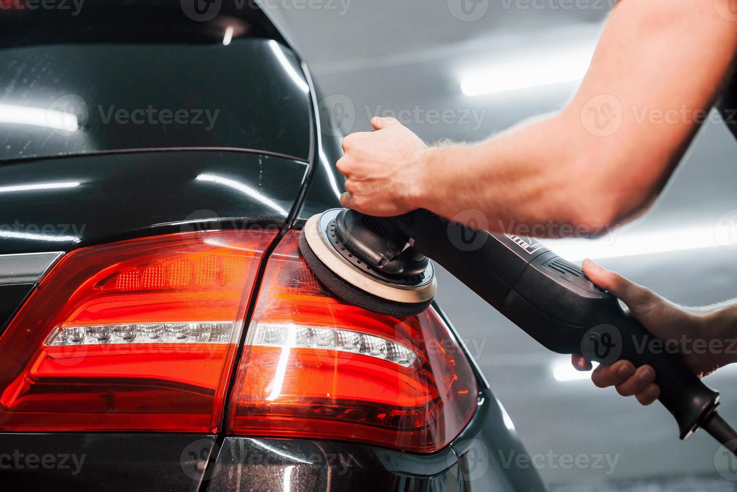 Guy polishing surface of vehicle. Modern black automobile get cleaned by man inside of car wash station photo