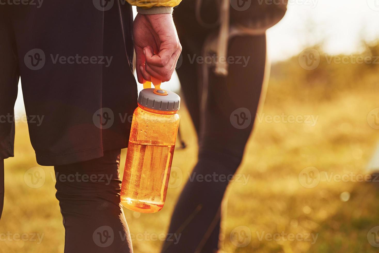 Close up view of couple that walking outdoors. Man holds bottle with water photo