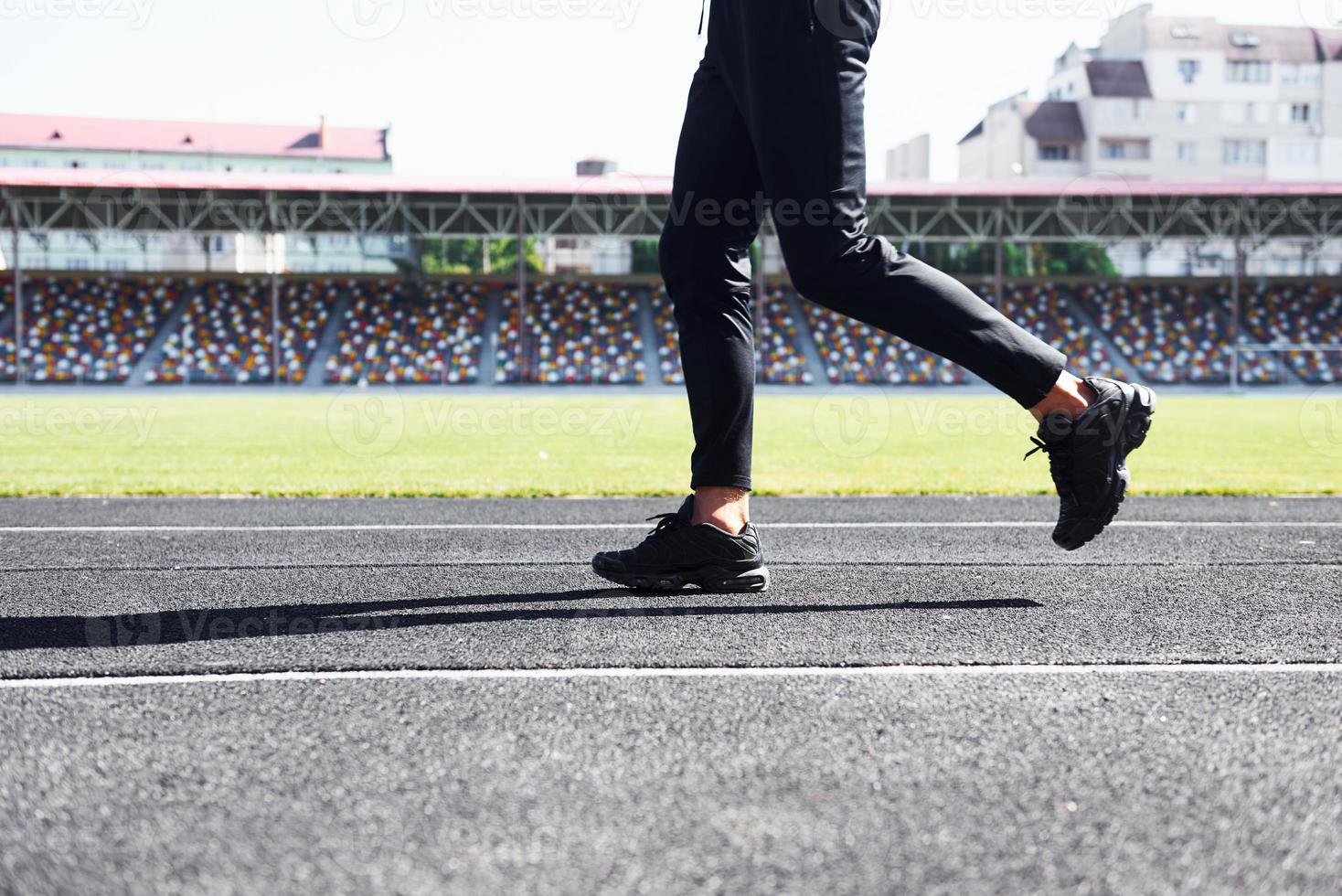 Close up view of legs of runner in black pants and shoes that is outdoors on the track photo