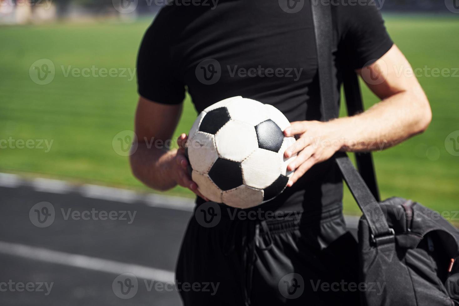 Football player on the field. Sportive young guy in black shirt and pants outdoors at daytime photo