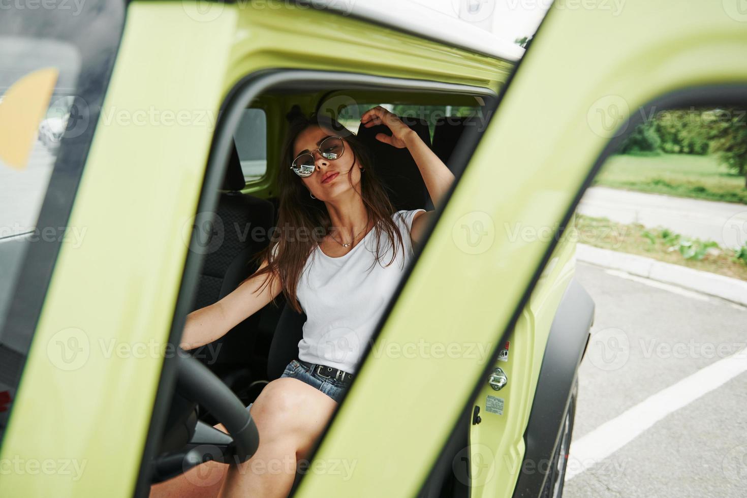 In sunglasses. Pretty woman in the green modern car posing for the camera photo
