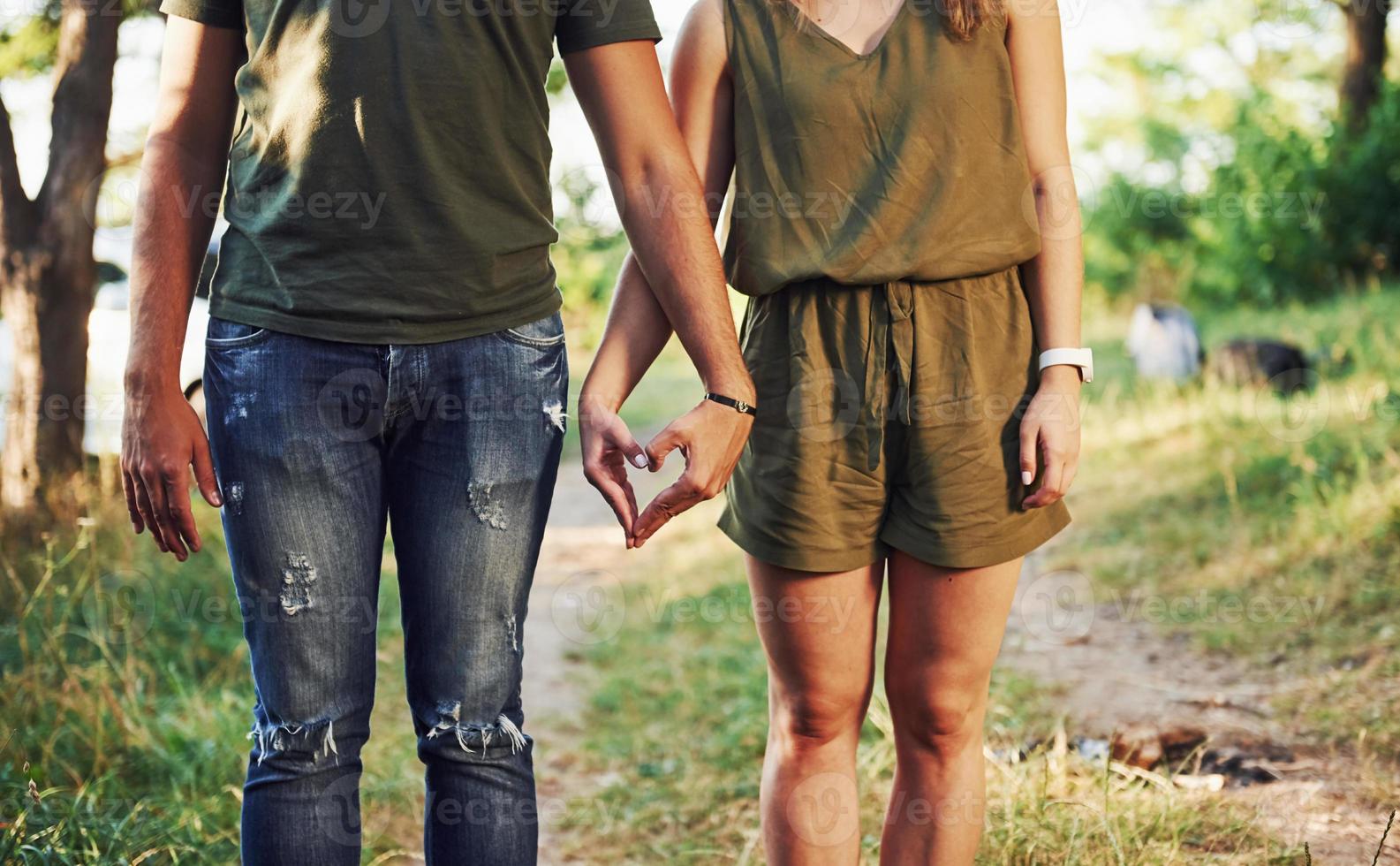 Making heart and love gesture by the hands. Young couple have a good time in the forest at daytime photo