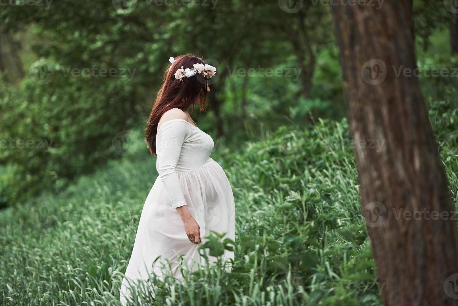 In the forest. Beautiful pregnant woman in dress have a walk outdoors. Positive brunette photo