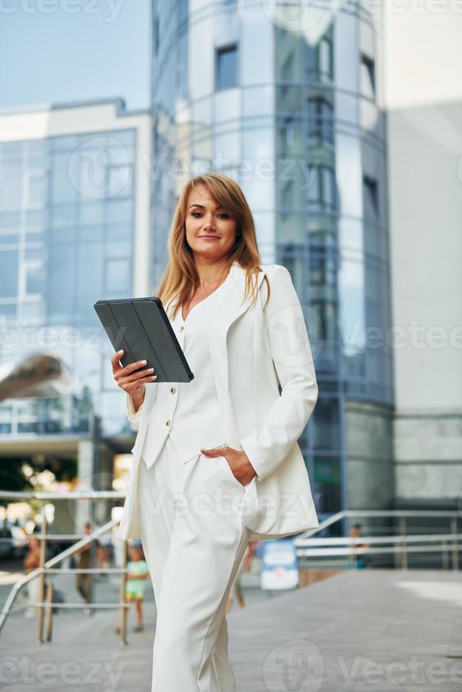 Against business building. Woman in formal wear standing outdoors in the city at daytime photo
