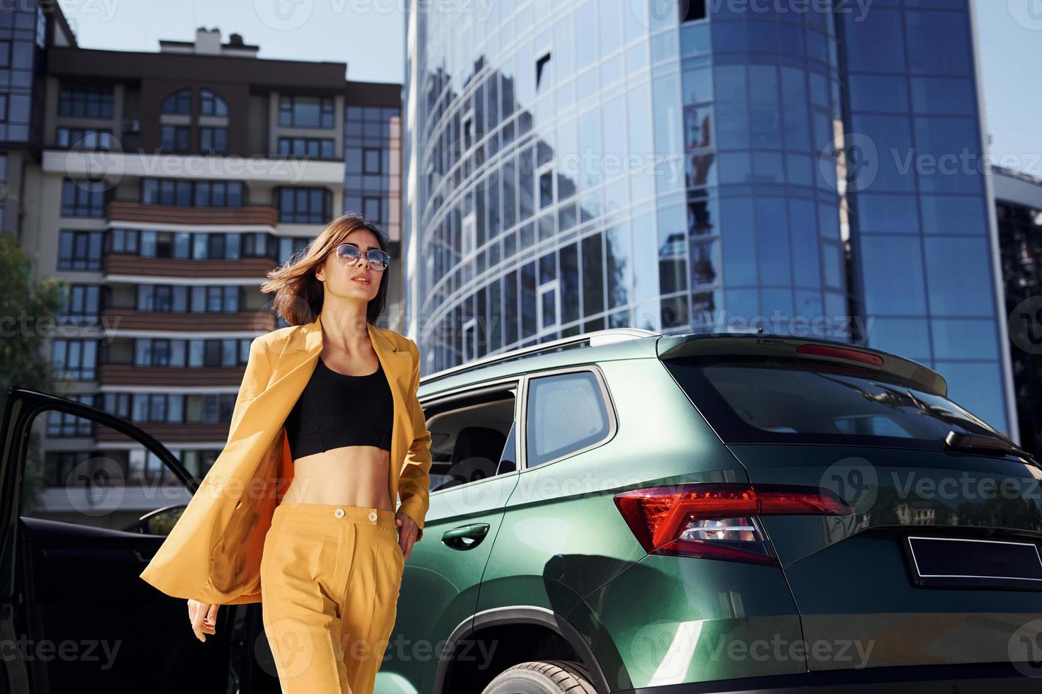 Walks forward from automobile. Young fashionable woman in burgundy colored coat at daytime with her car photo