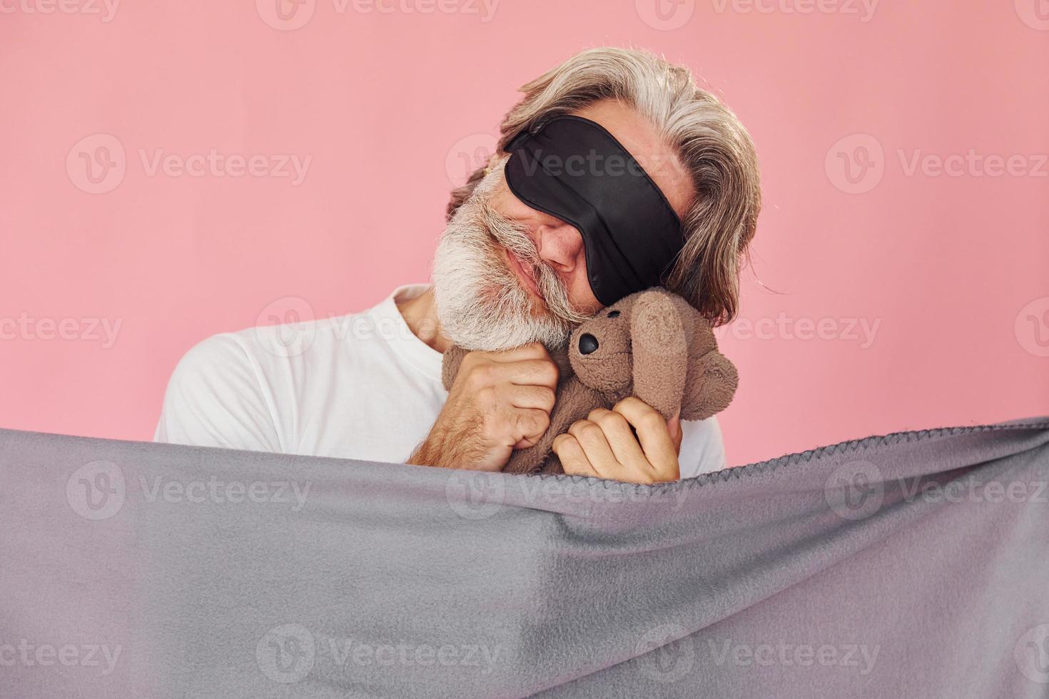 Holds teddy bear. Stylish modern senior man with gray hair and beard is indoors photo