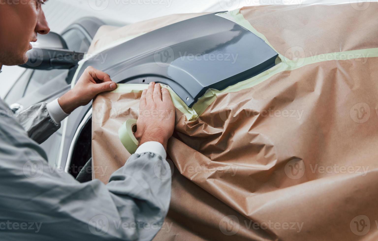 Covering car by brown cloth. Caucasian automobile repairman in uniform works in garage photo