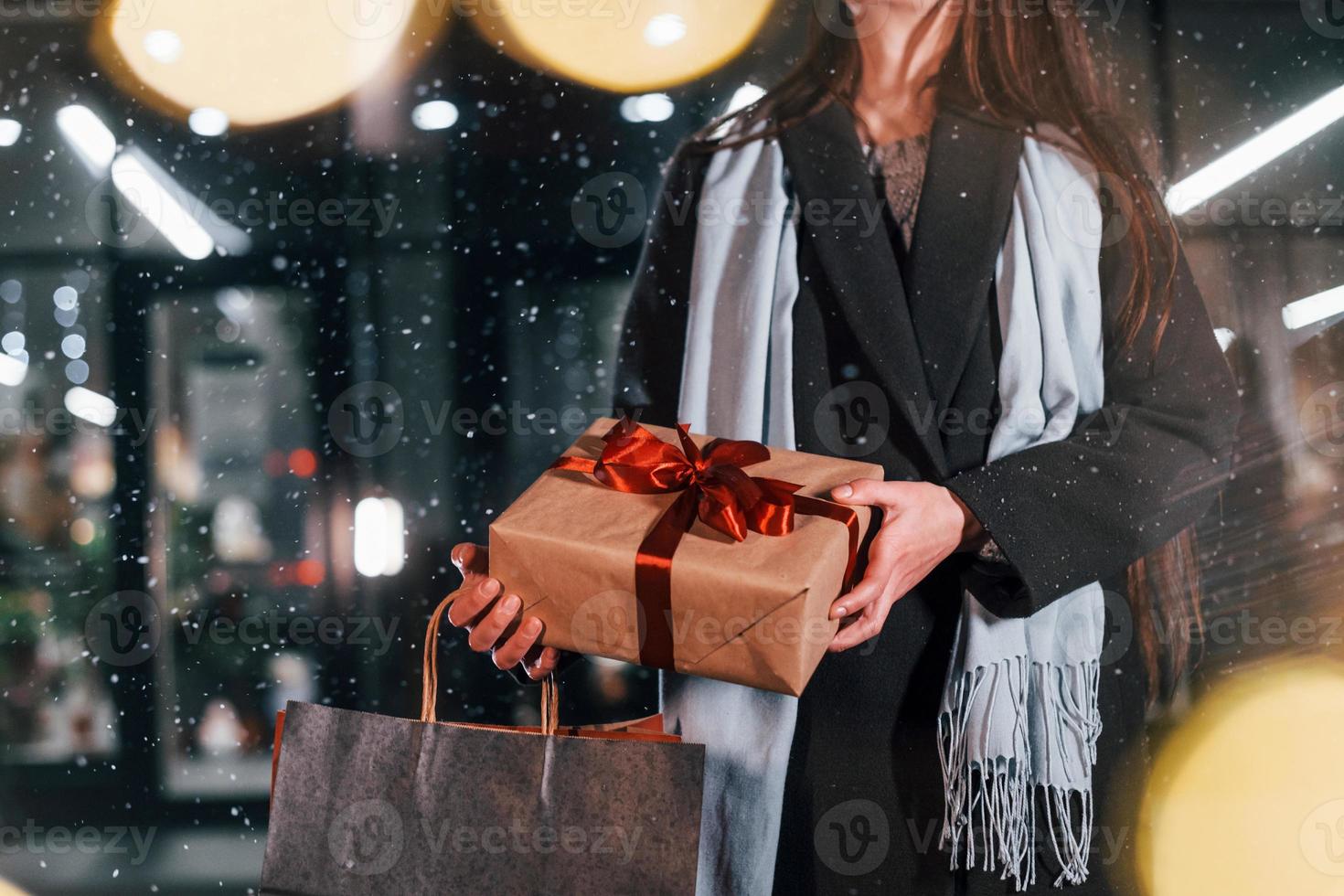 From the shop with gift box in hands. Cheerful woman is outdoors at Christmas holidays time. Conception of new year photo