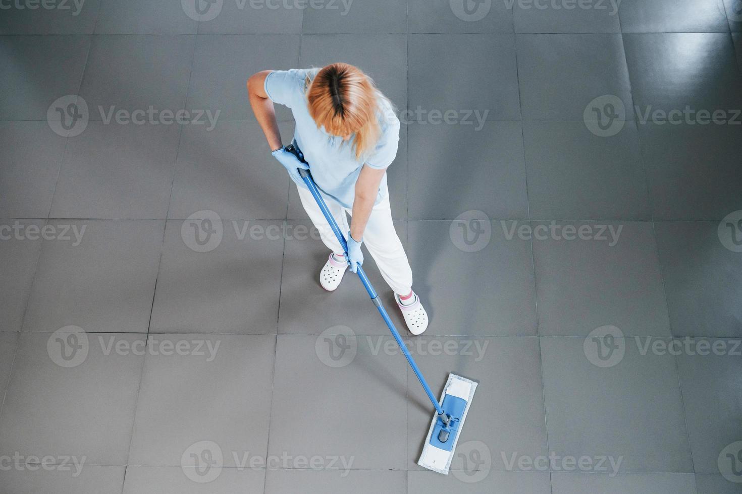 Top view of woman in blue shirt and protective gloves that uses vacuum cleaner photo