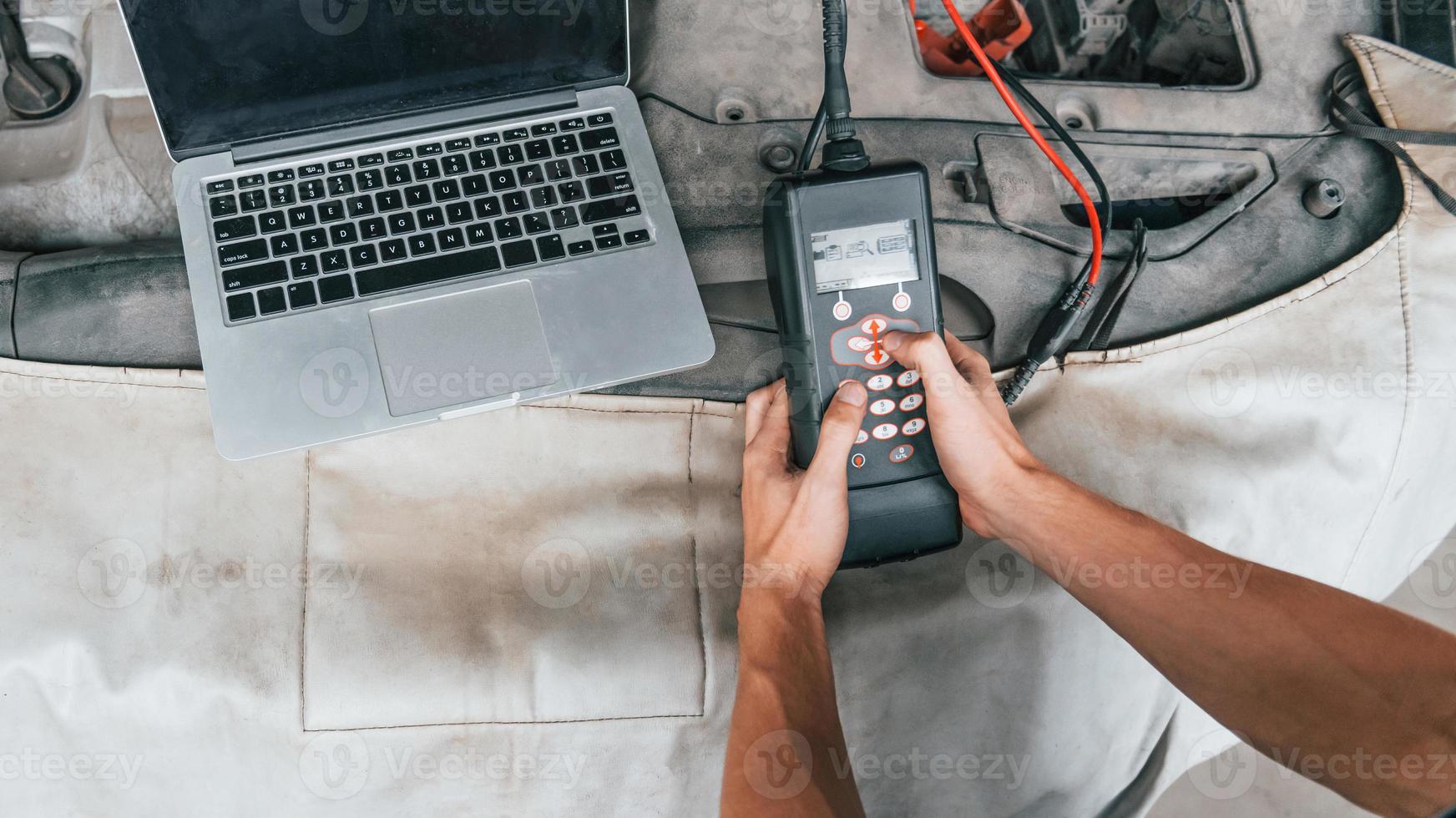 Close up view of man's hands that holding device for testing automobile in salon photo