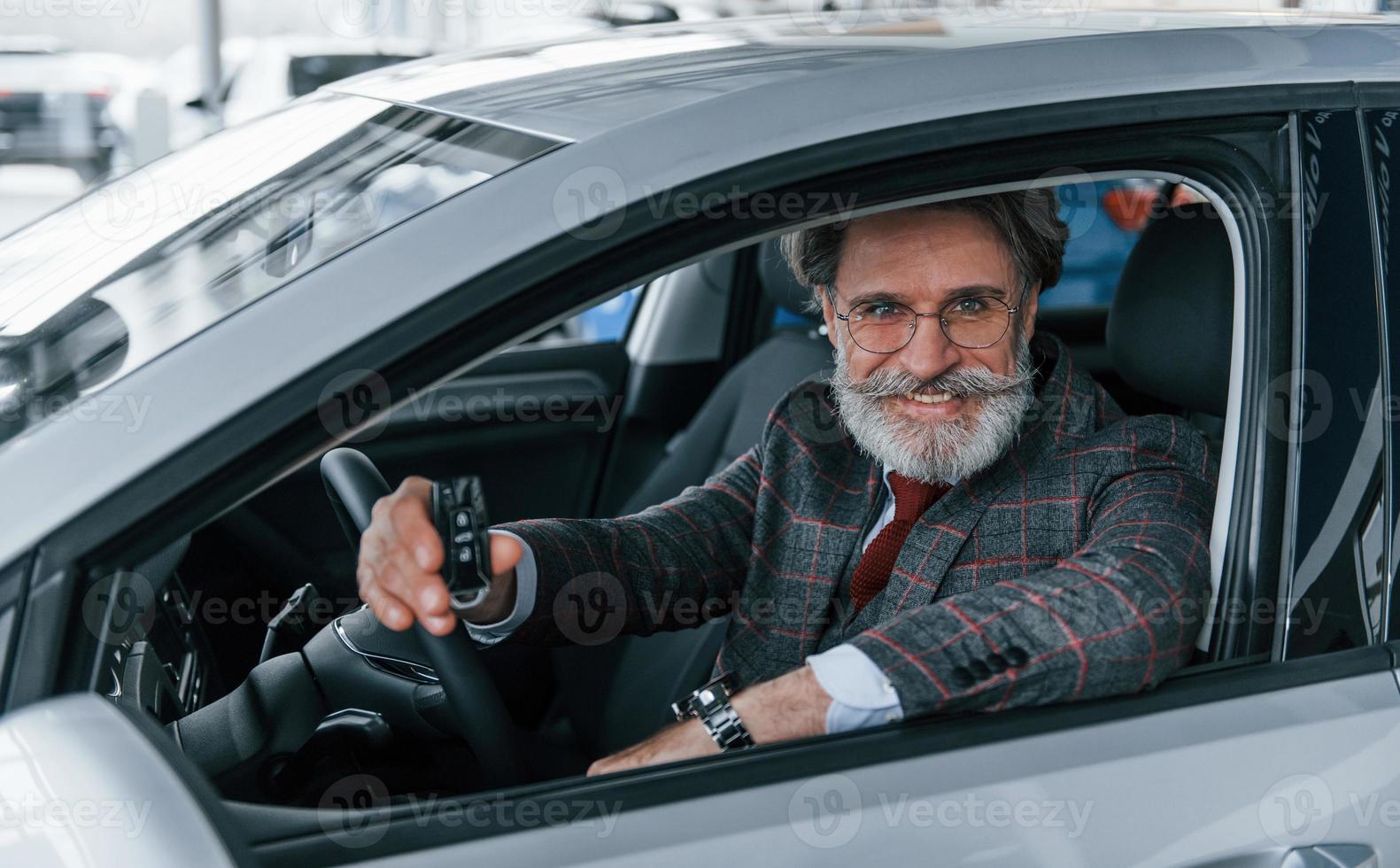 Modern stylish senior man with grey hair and mustache holding keys in modern car photo