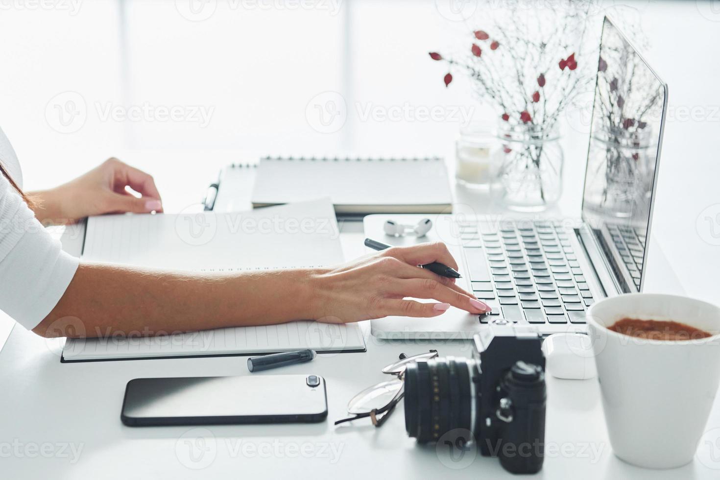 Using laptop and notepad. Young female freelancer working indoors in the office at daytime photo